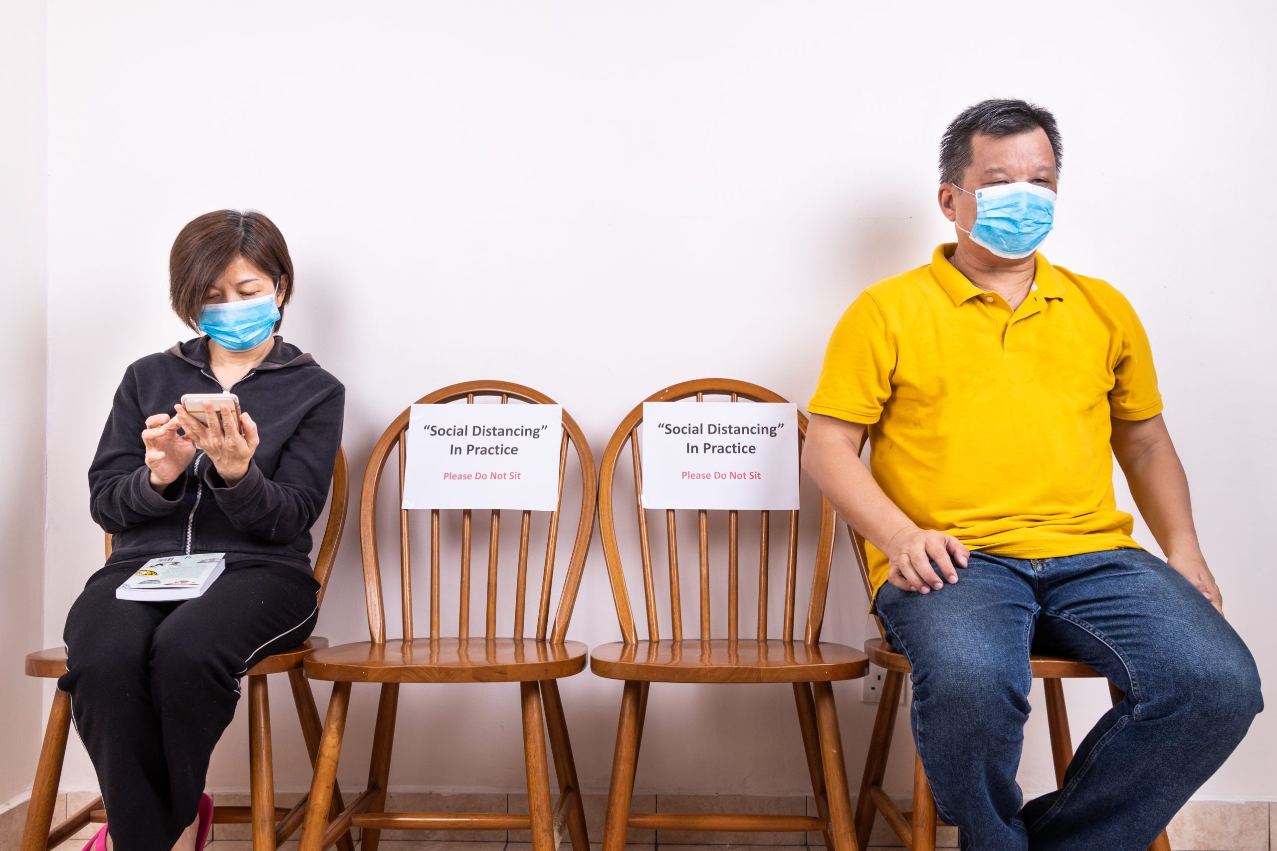 People with face mask seated in-between two chairs at public place, with Social Distancing, Do Not Sit signage to prevent spread of Covid-19 pandemic Social Distancing
